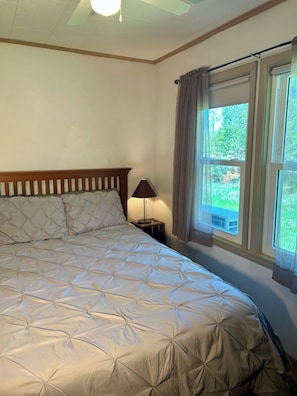 Une chambre à coucher avec un lit, une table de chevet, une lampe et une fenêtre avec des rideaux.