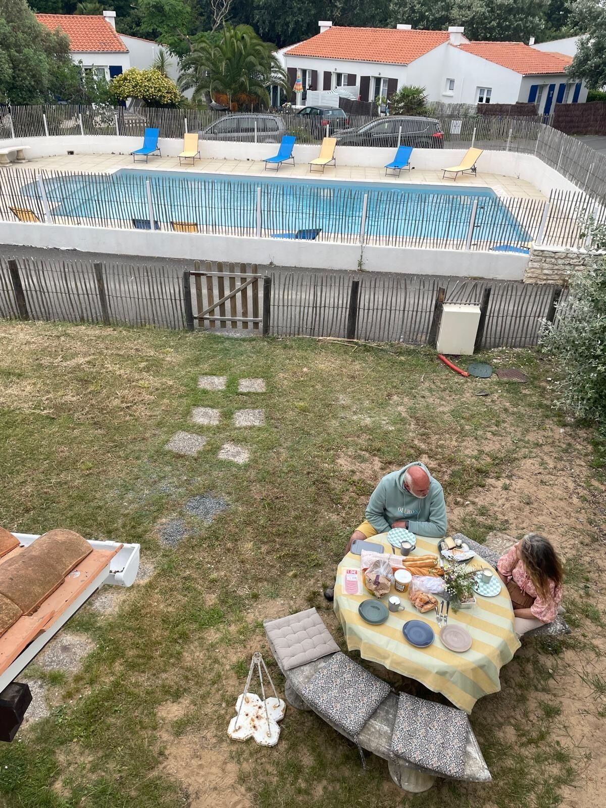 A backyard with a swimming pool, a table set for a meal, and a fenced area with lounge chairs.