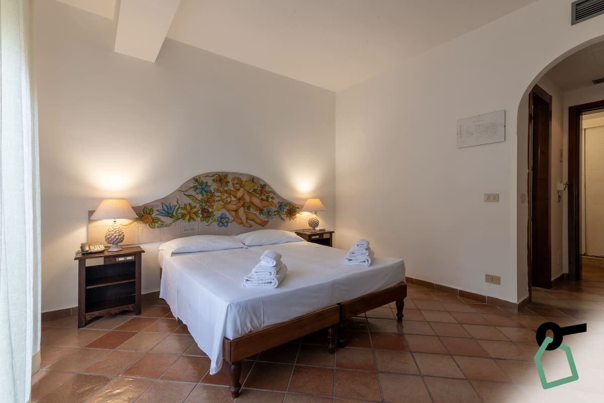 A hotel room with a bed, two bedside lamps, a nightstand, and a floral headboard.