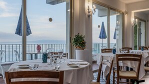 A restaurant with tables set for dining, a potted plant, and a view of the sea. - Hotiday Taormina Mare (Taormina)