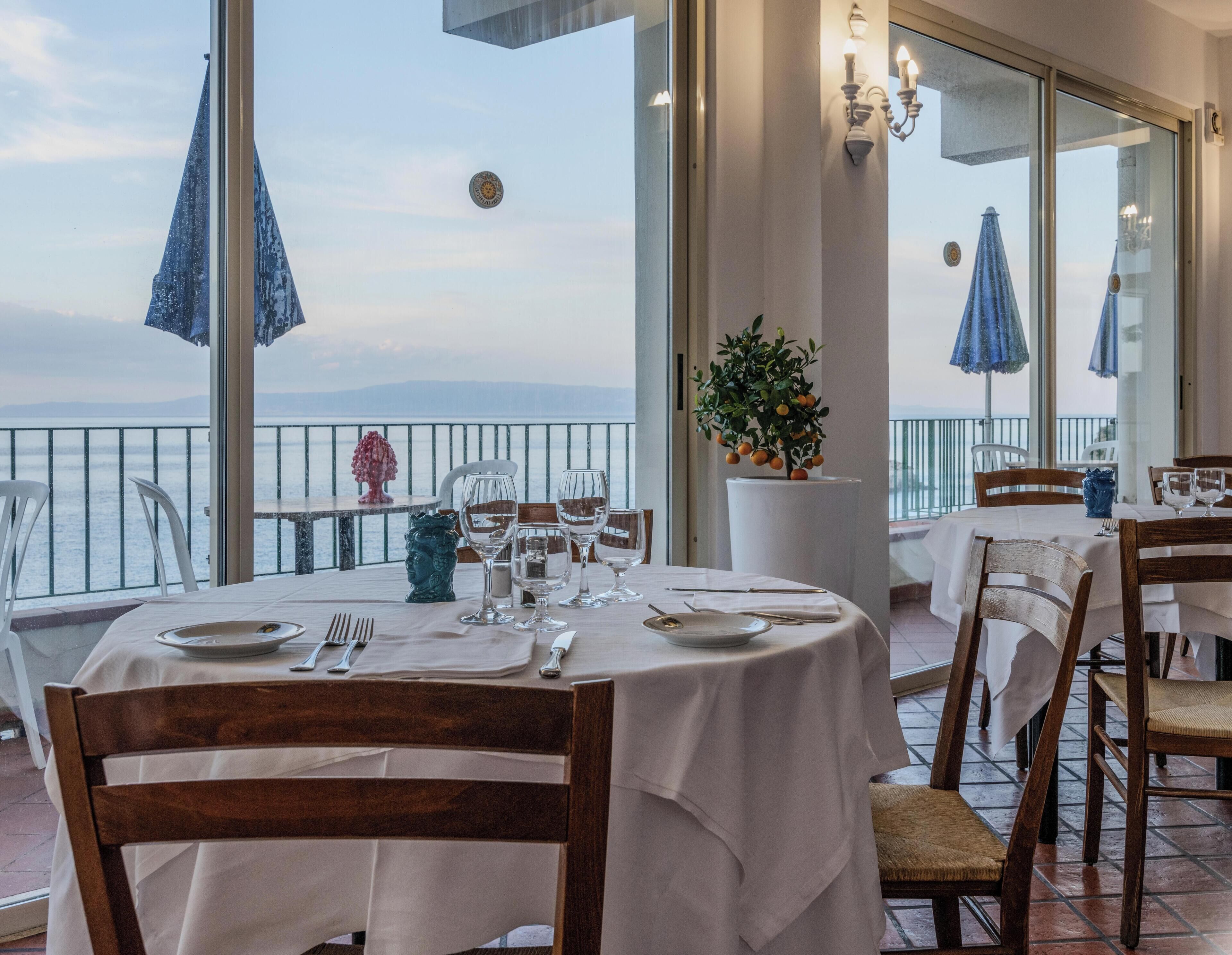 Un restaurant avec des tables dressées, une plante en pot et une vue sur la mer.
