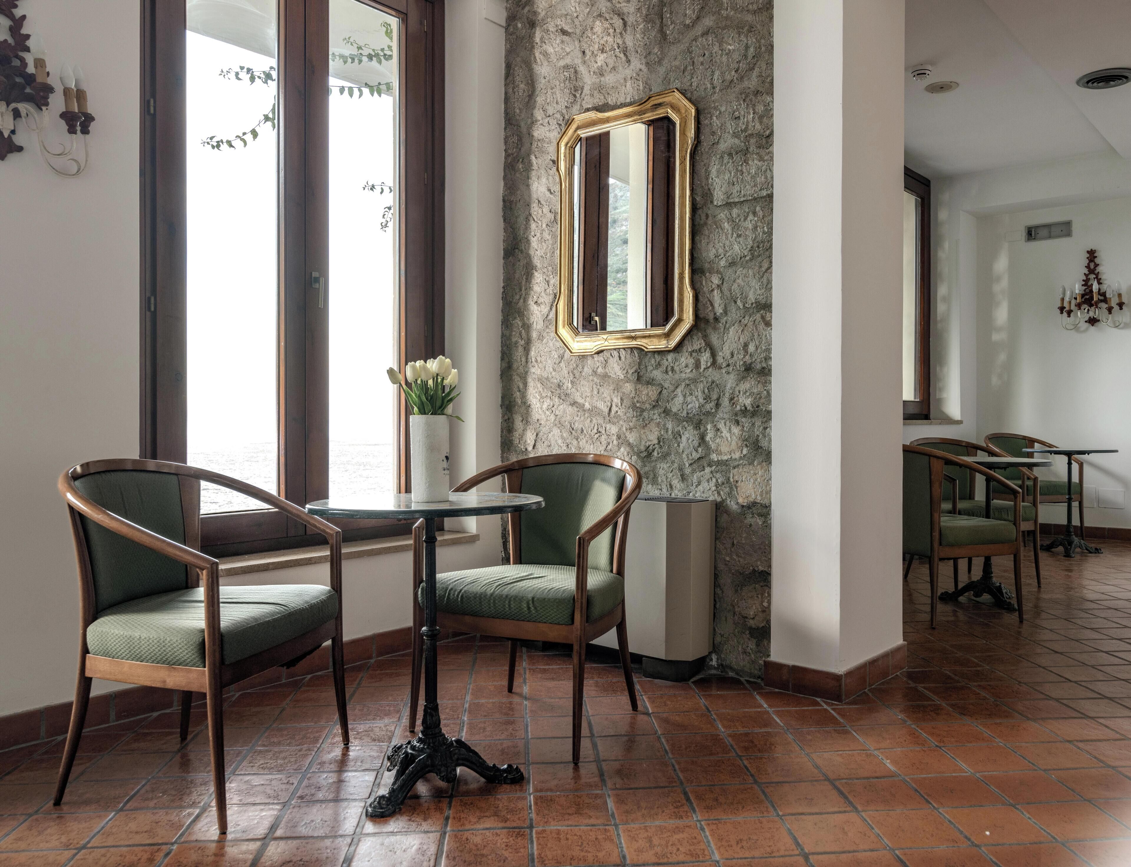 Una habitación con dos sillas, una mesita, un espejo en una pared con textura y una ventana con vistas.