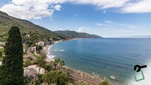 A coastal landscape with a clear view of the sea, a railway track, and a small settlement with buildings and greenery. - Hotiday Taormina Mare (Taormina)