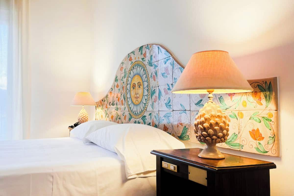 A hotel room with a bed, a nightstand with a lamp, a telephone, and a decorative headboard.