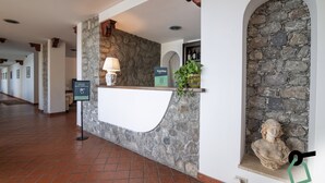 A hotel reception area with a stone wall, a reception desk, a sign for room collection, a statue, and a plant. - Hotiday Taormina Mare (Taormina)