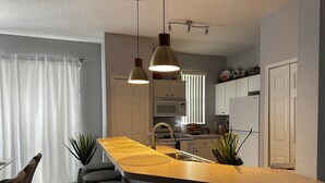 A modern kitchen with a curved island, pendant lighting, and a dining area with bar stools. - Cozy townhouse close to Disney, Universal parks, restaurant with prkg free (Kissimmee)