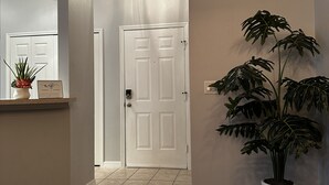 A hallway with a white door, a potted plant, and a sign on a shelf. - Cozy townhouse close to Disney, Universal parks, restaurant with prkg free (Kissimmee)