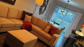 A living room with a sectional sofa, a coffee table, and a dining area with chairs. - Cozy townhouse close to Disney, Universal parks, restaurant with prkg free (Kissimmee)