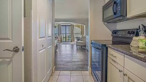 A kitchen with a microwave, stove, and cabinets. There is a dining area with a chair and a table.