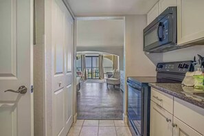 A kitchen with a microwave, stove, and cabinets. There is a dining area with a chair and a table.