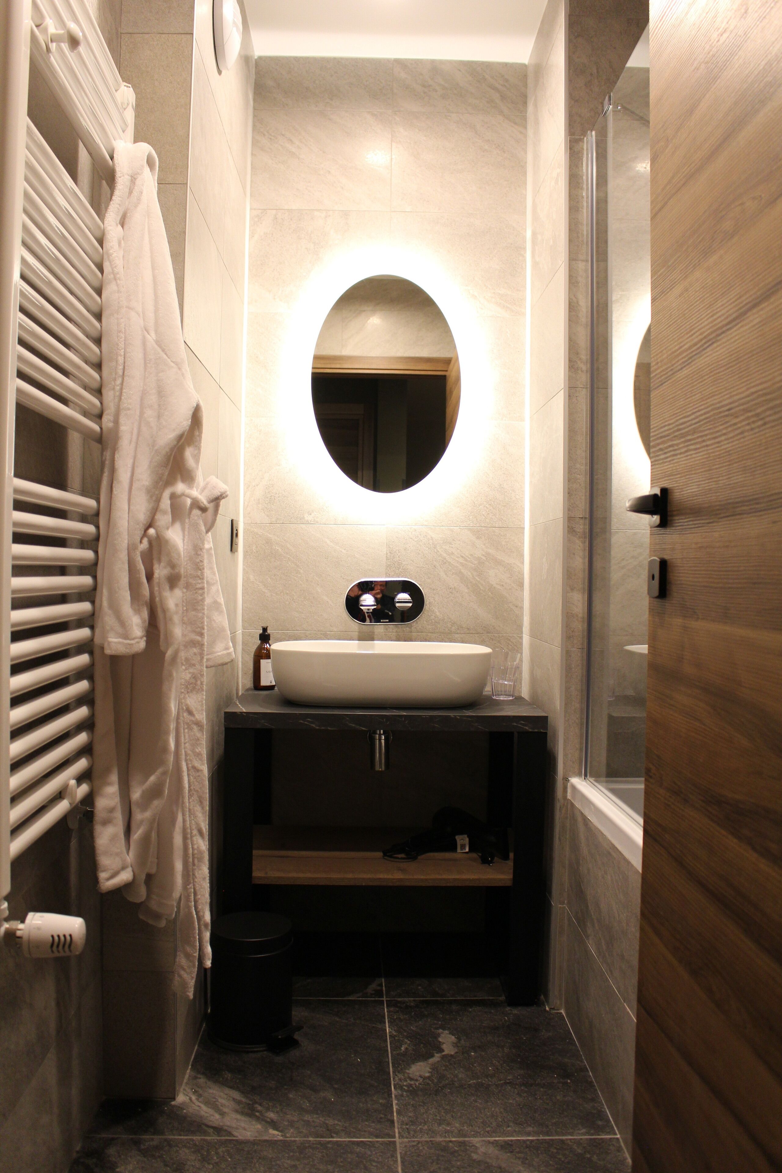 A modern bathroom with a large oval mirror, a white sink, and a towel rack.