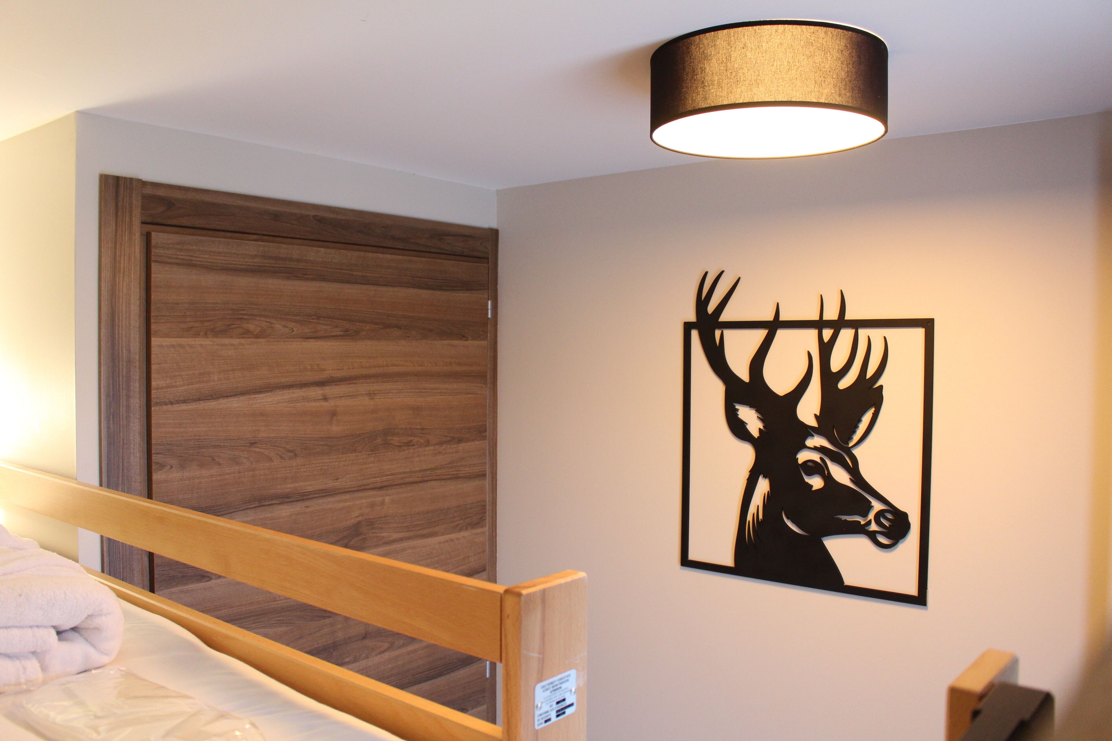 A bedroom with a wooden bed frame, a wall-mounted lamp, and a framed deer artwork.