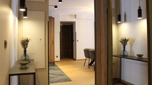 A modern interior with a wooden floor, a dining area with chairs, a vase with flowers on a console table, and pendant lighting. - Les Cîmes d'Auréa (Valloire)