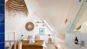Een moderne slaapkamer met een bed, nachtkastjes, een hanglamp, een wandspiegel en een badkamer met een wastafel en spiegel.