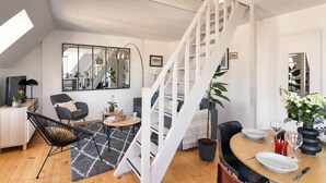 Een moderne leefruimte met een trap, een eethoek en een zithoek met een zwarte stoel en een klein tafeltje.