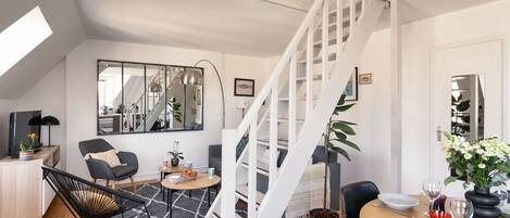 Un espacio de estar moderno con una escalera, un comedor y una zona de asientos con una silla negra y una mesita.