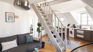 Een modern appartement met een trap naar een hoger niveau, een keuken met een wasmachine, en een zithoek met een bank en salontafel.