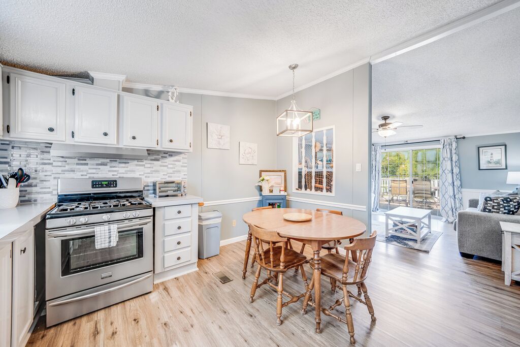 A modern kitchen with white cabinets, a stainless steel stove, and a dining area with wooden chairs.