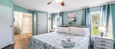 Un dormitorio con cama, ventilador de techo, mesita de noche, lámpara y vistas al exterior.