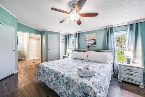 Une chambre à coucher avec un lit, un ventilateur de plafond, une table de chevet, une lampe et une vue sur l’extérieur.