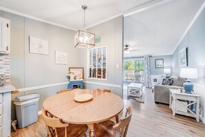 A dining area with a round wooden table and chairs, a hanging light fixture, and a view into the living room.