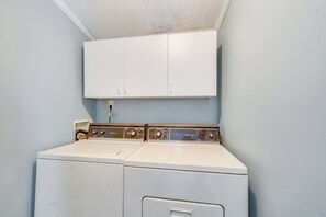 A laundry room with a front-loading washer and dryer, a white cabinet above, and a light blue wall. - Bayside Haven by Seaside Vacations & Sales (Chincoteague Island)