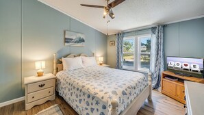 A bedroom with a bed, nightstands, a ceiling fan, a TV, and a window with curtains. - Bayside Haven by Seaside Vacations & Sales (Chincoteague Island)