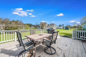 A wooden deck with a table and chairs, surrounded by white railings. - Bayside Haven by Seaside Vacations & Sales (Chincoteague Island)