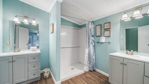 A bathroom with two sinks, a shower, and a vanity with drawers. - Bayside Haven by Seaside Vacations & Sales (Chincoteague Island)