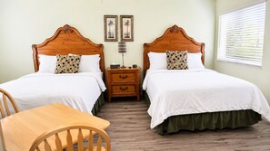 A room with two wooden beds, a wooden chair, a nightstand, and a window with blinds.