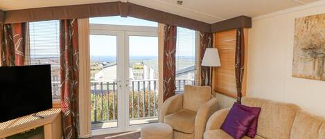 A living room with a television, sofa, and armchair, a balcony with a view, and a lamp.