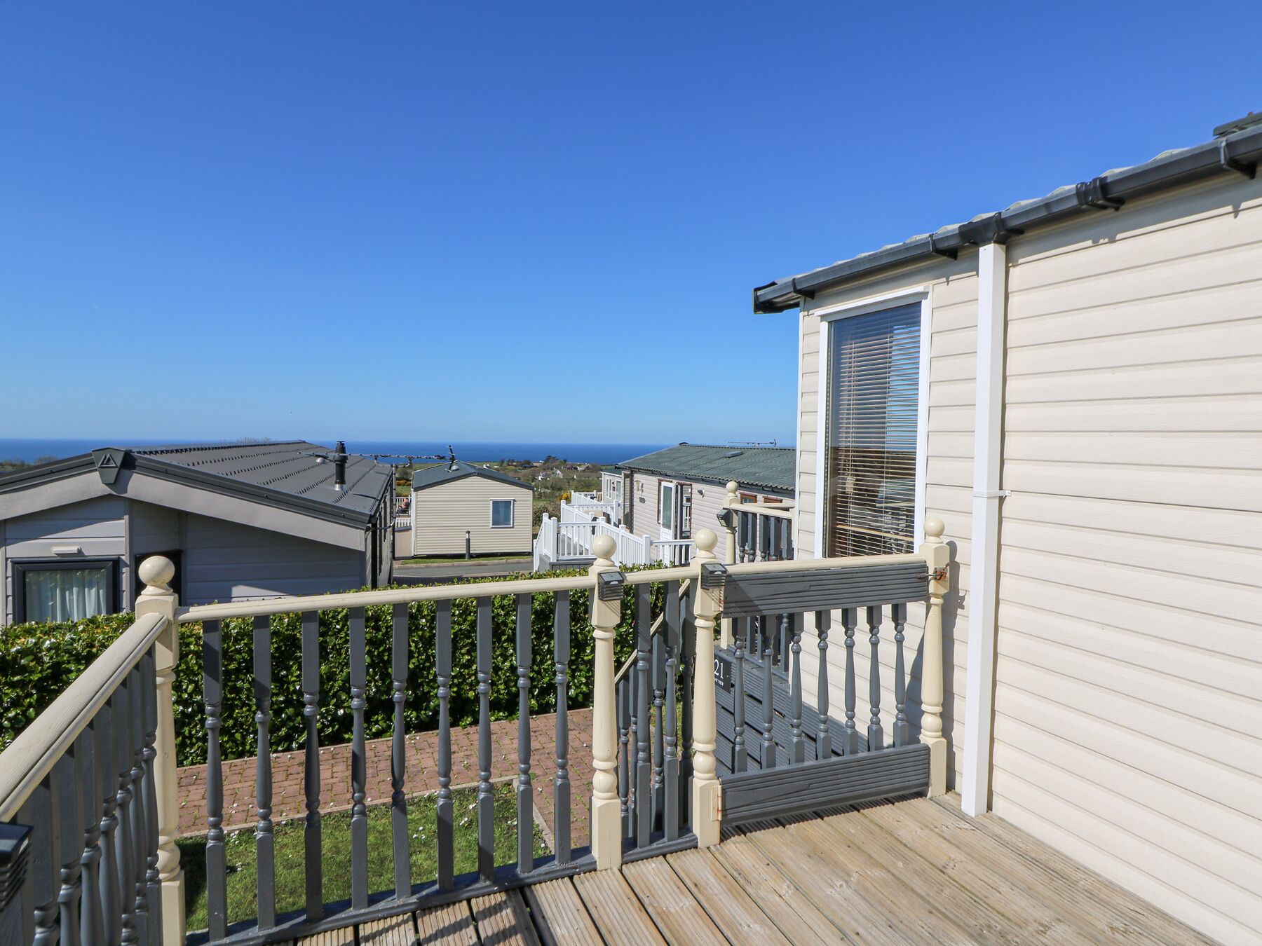 A wooden deck with a railing, leading to a white building with a large window and a door.