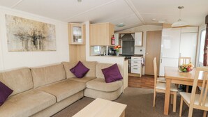 Ett kompakt bostadsutrymme med en soffa, ett litet bord, en köksdel med skåp och en spis samt ett matbord med stolar.