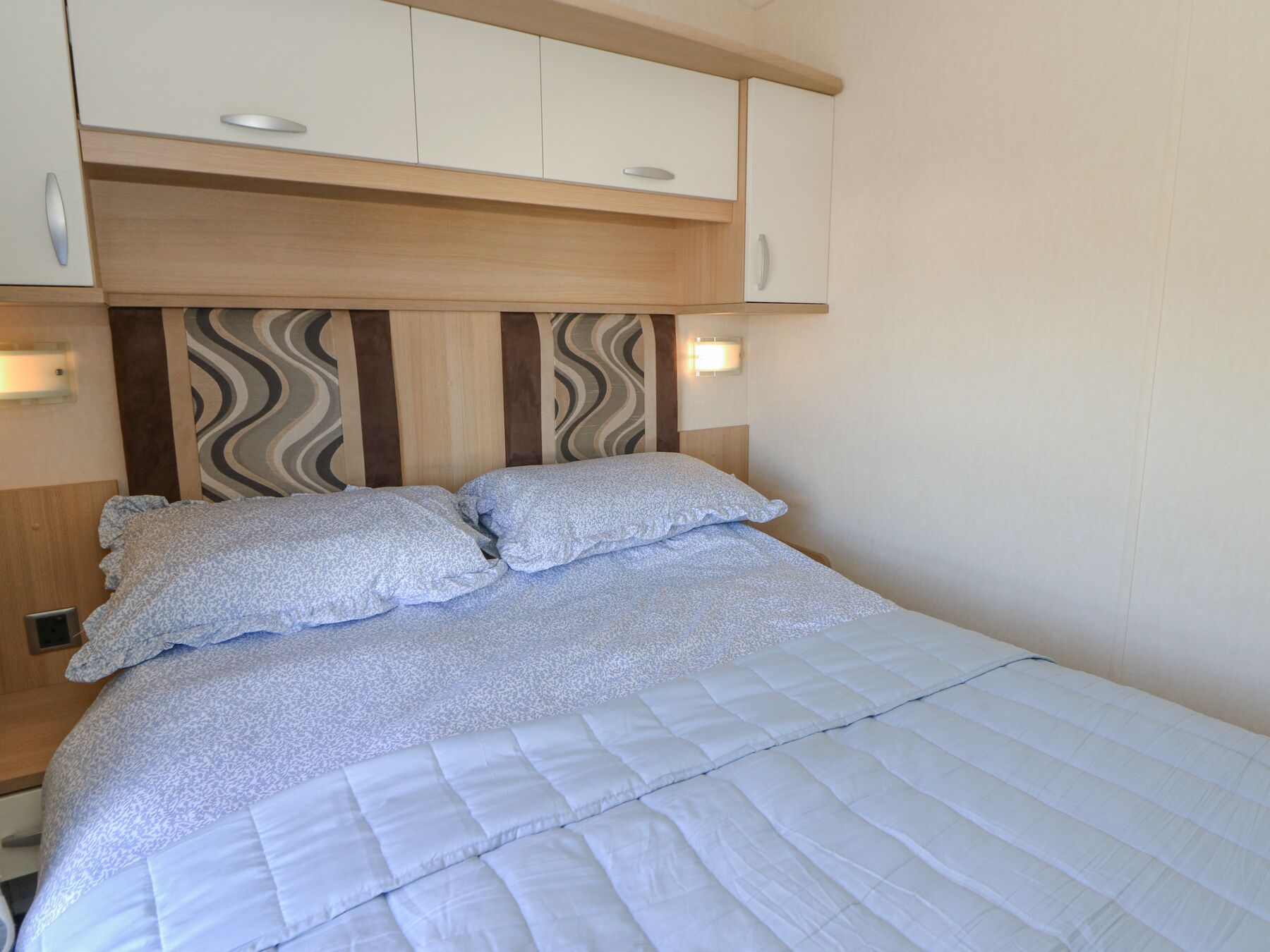 Cama com cobertura branca acolchoada, duas almofadas e cabeceira com padrão ondulado.