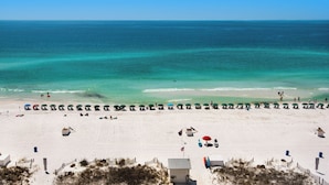A beach with rows of umbrellas and beach chairs, a lifeguard tower, and a sandy shoreline.
