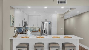 A modern kitchen with white cabinetry, stainless steel appliances, and a central island with bar stools.