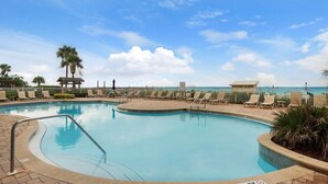 A swimming pool with lounge chairs and a palm tree, surrounded by a fence, with a view of the beach and ocean.