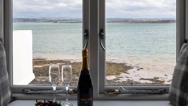 A window view of a coastal area with a bottle of wine and glasses on a table.