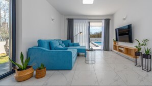 A modern living room with a sectional sofa, a flat-screen TV, and a large window offering a view of the outdoors. - Villa Merci ZadarVillas (Privlaka)
