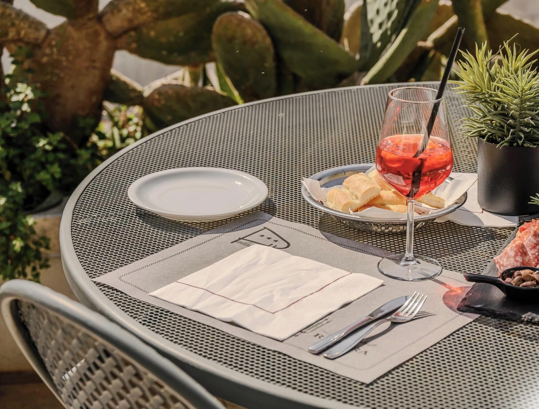 A round metal table with a white plate, a glass of red drink, bread, and cutlery.