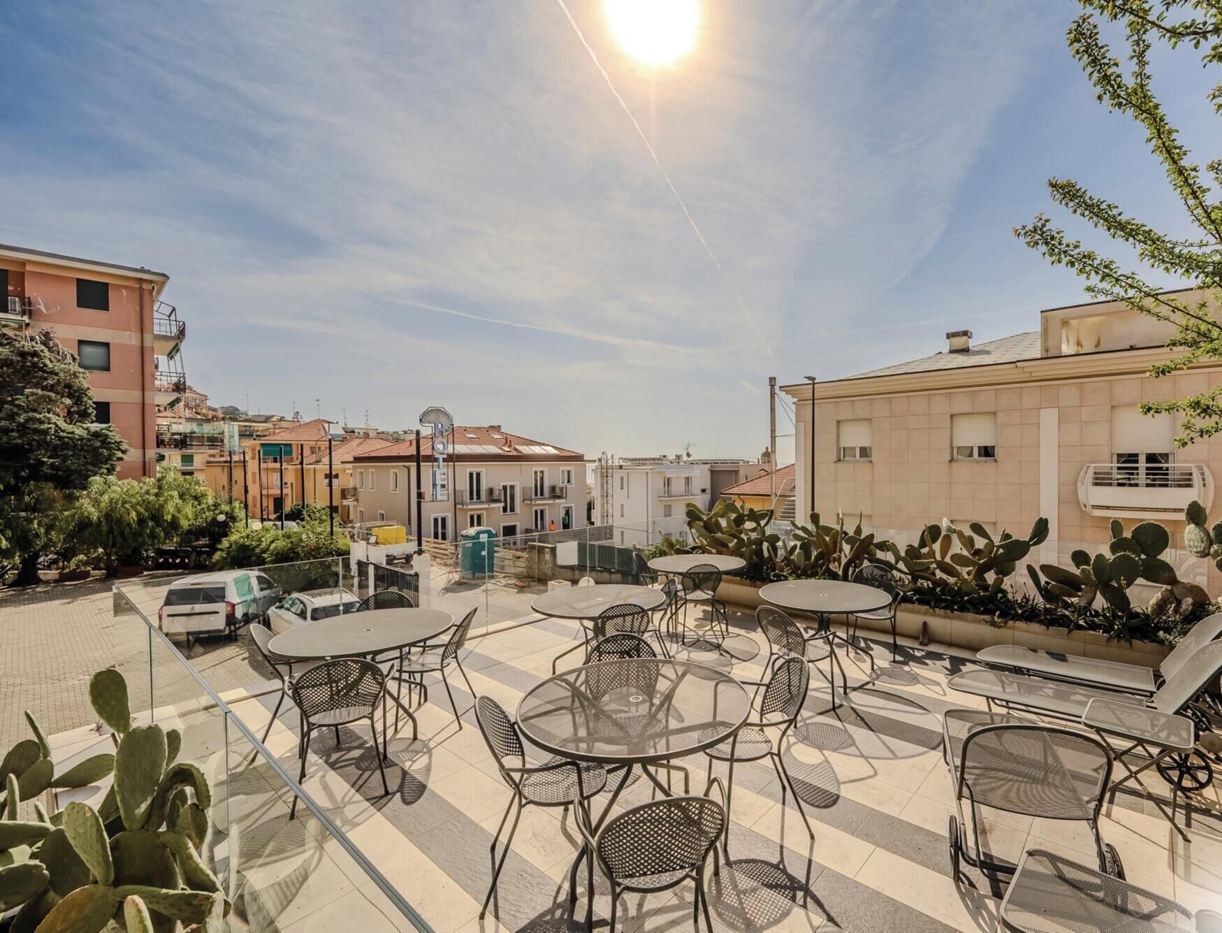 A rooftop terrace with outdoor seating, a clear sky, and surrounding buildings.
