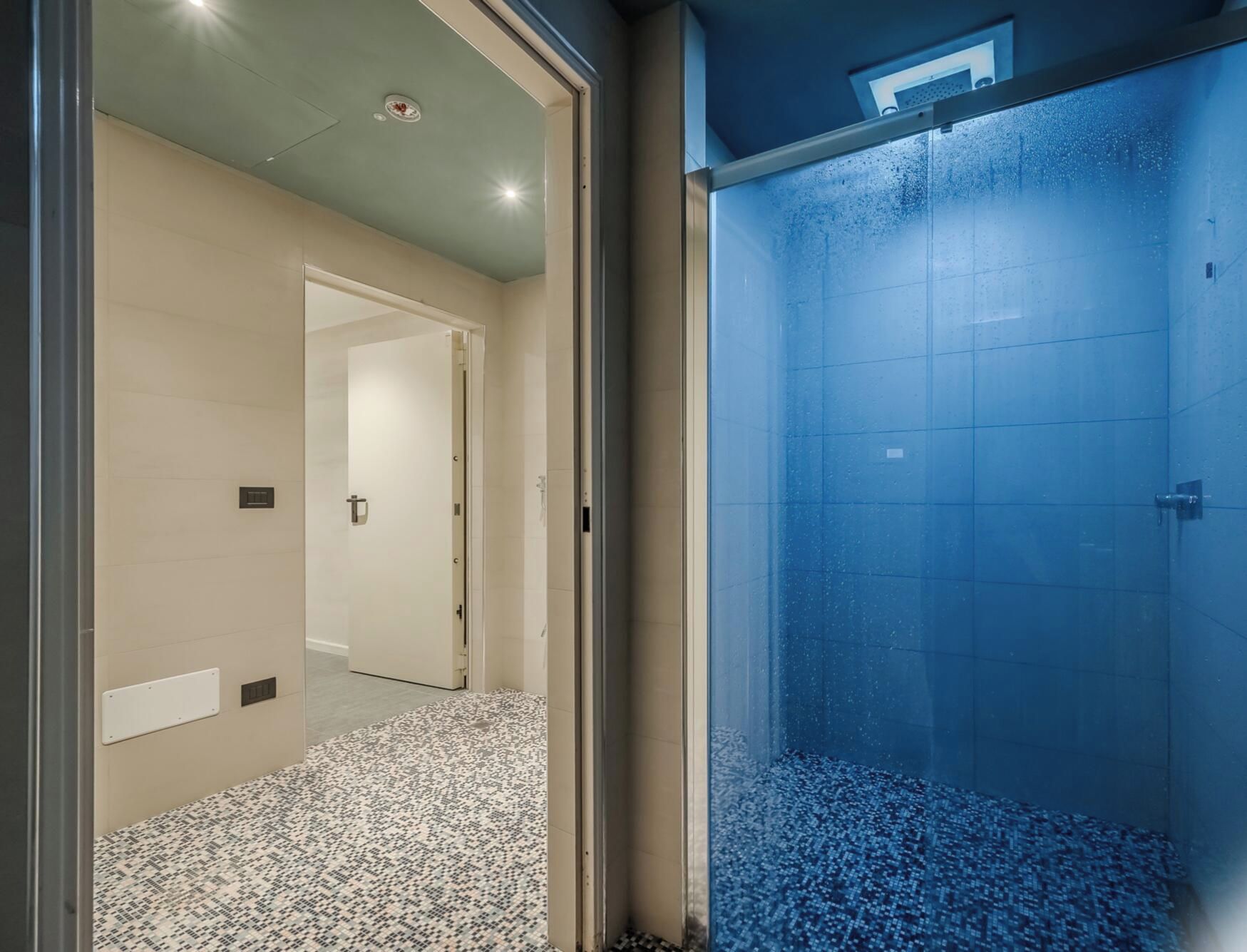 Un couloir d’hôtel moderne avec une porte en verre donnant accès à un espace douche.