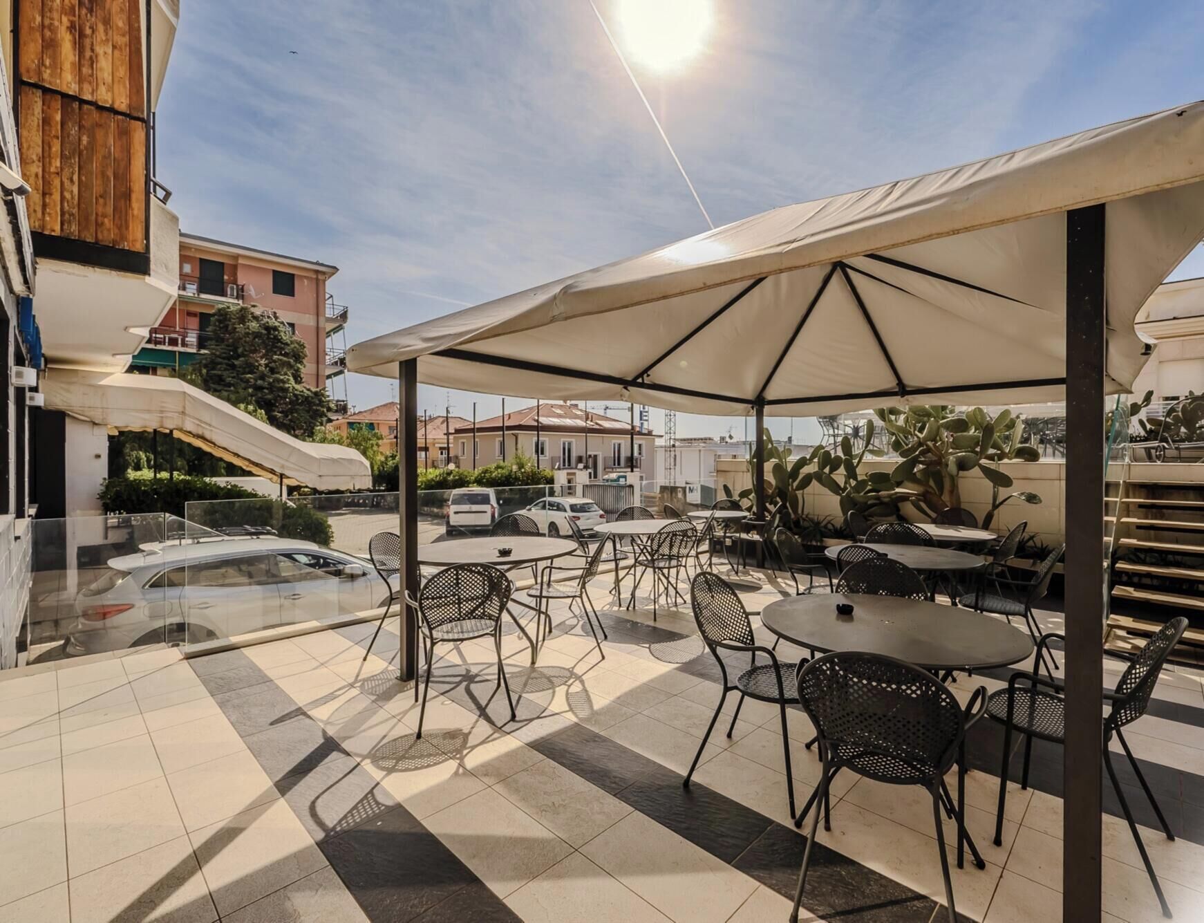 Un patio exterior con mesas y sillas, una zona de estar cubierta y vistas de los edificios circundantes.