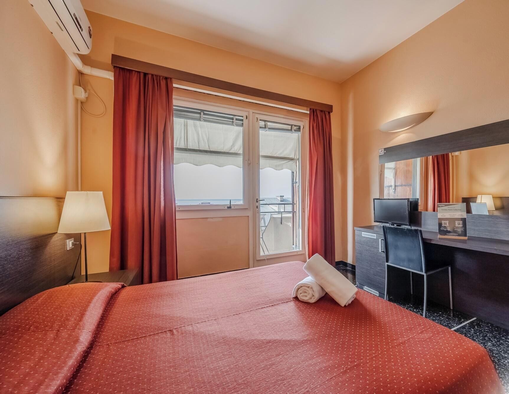 Ein Hotelzimmer mit Bett, Schreibtisch, Stuhl, Fernseher und einem Fenster mit Vorhängen.