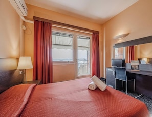 A hotel room with a bed, a desk, a chair, a TV, and a window with curtains.