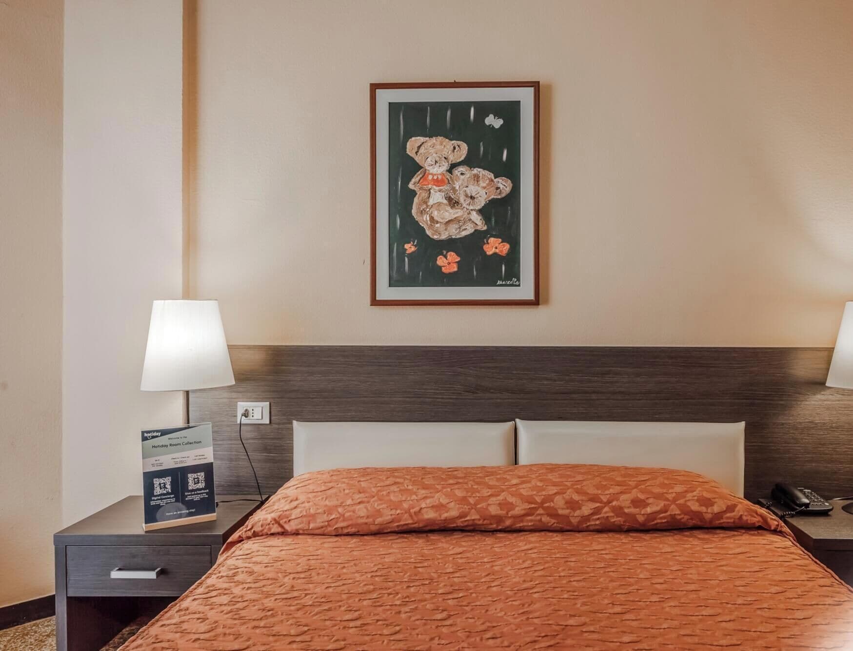 Quarto de hotel com cama, mesa de cabeceira com luminária, quadro na parede e placa sobre a coleção de quartos temáticos.