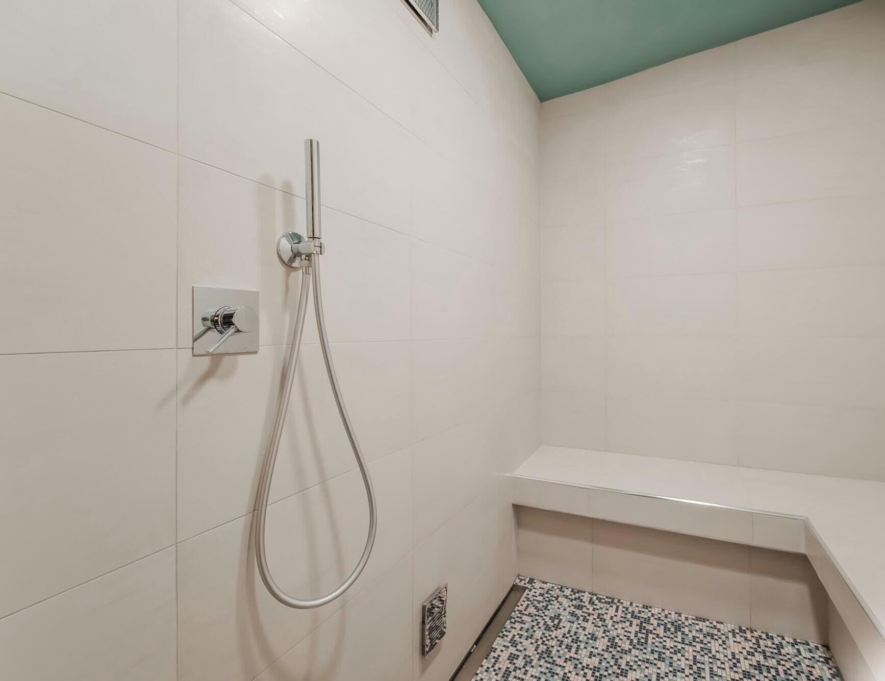 A bathroom with a shower, a towel rack, and a patterned floor mat.