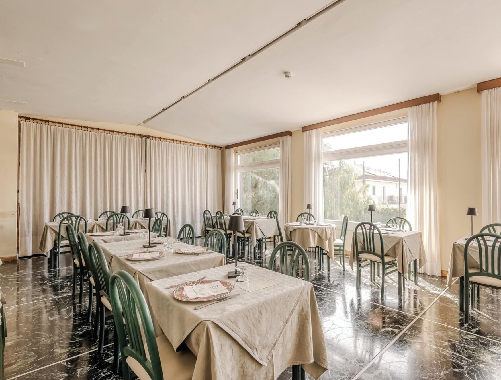 A dining area with tables set for service, chairs, and a large window providing natural light.