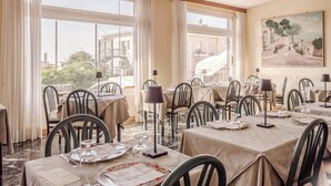 A dining area with tables set for service, large windows with curtains, and a landscape painting on the wall.