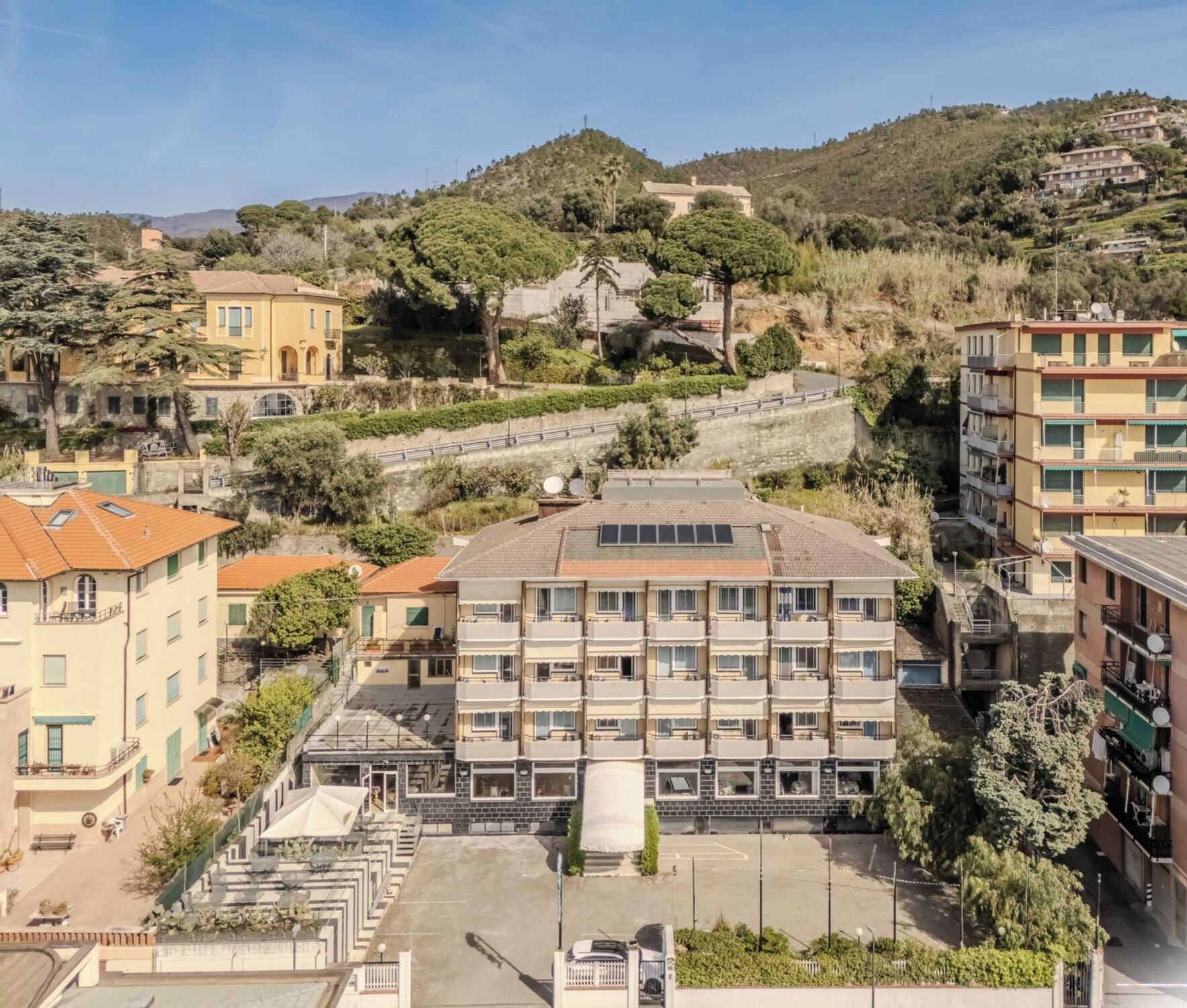 Un immeuble à plusieurs étages doté d’une cour intérieure, entouré d’immeubles d’habitation et avec des collines en arrière-plan.